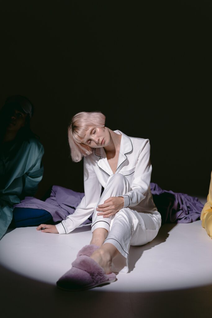 femme avec un pyjama en satin et des chaussons rose assise sur un lit